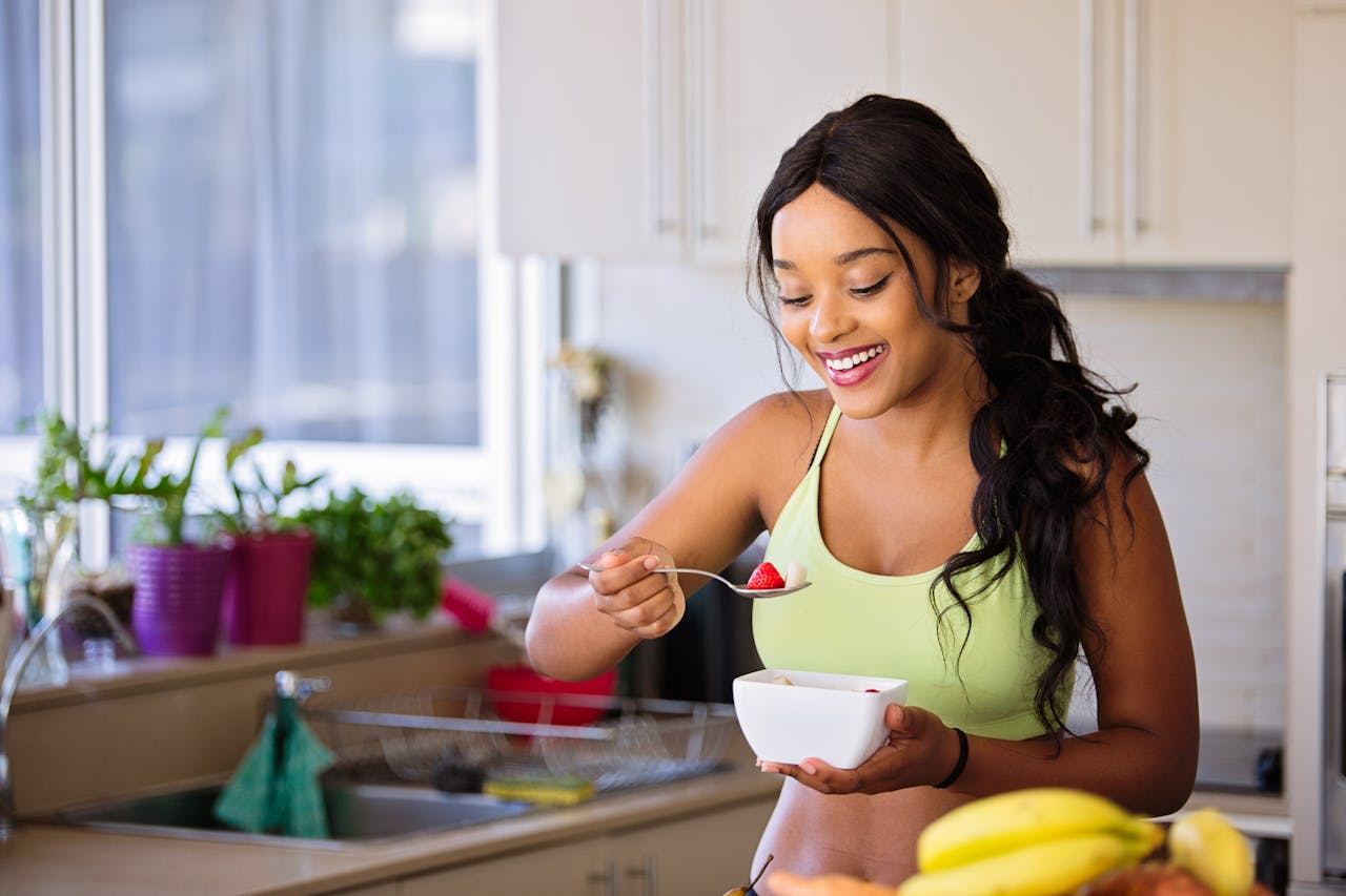 Smiling woman eating a nutritious fruit bowl in a bright kitchen setting.