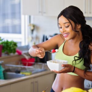 Cheerful woman enjoying fresh strawberries in a cozy kitchen setting. Promotes healthy living and happiness.