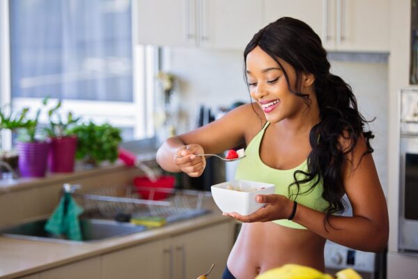 Cheerful woman enjoying fresh strawberries in a cozy kitchen setting. Promotes healthy living and happiness.