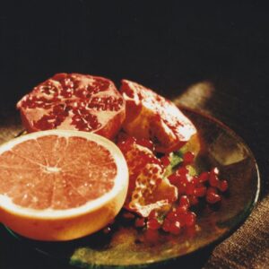 A still life composition of grapefruit and pomegranate on a plate in natural sunlight.