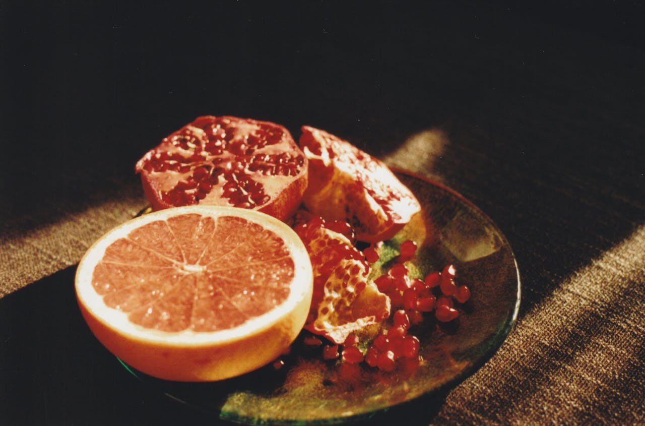 A still life composition of grapefruit and pomegranate on a plate in natural sunlight.